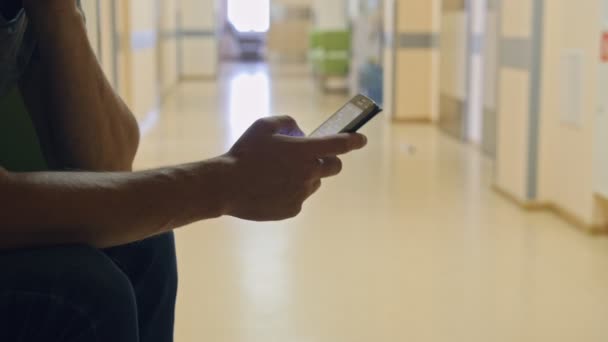 Hombre esperando en el hospital y el uso de teléfonos inteligentes, dilación — Vídeos de Stock