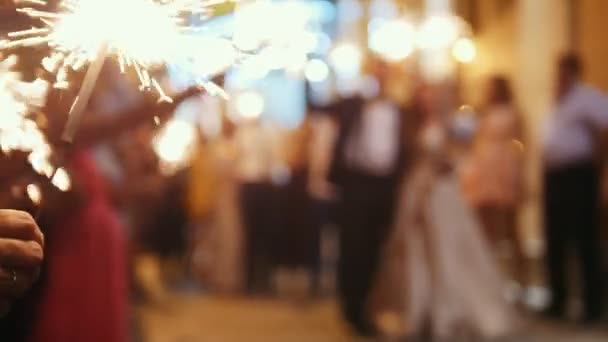 Sparkler in hands on a wedding - bride, groom and guests holding lights in, defocused — Stock Video