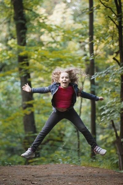 公園で少し笑みを浮かべて少女子身に着けているジーンズのジャケット - をジャンプします。 — ストック写真