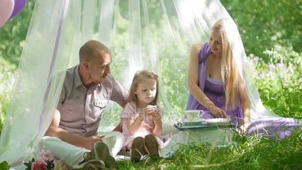 La familia está descansando en el parque - padre, madre e hija desayunan — Vídeo de stock