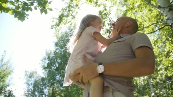 Feliz padre abrazando y balanceando a sus hijas en el parque, cámara lenta — Vídeo de stock