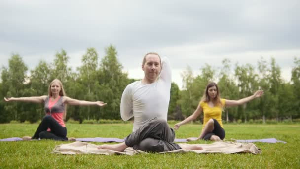 Entrenamiento de yoga al aire libre en el parque: el hombre y dos hermosos modelos de fitness realizan los ejercicios — Vídeo de stock