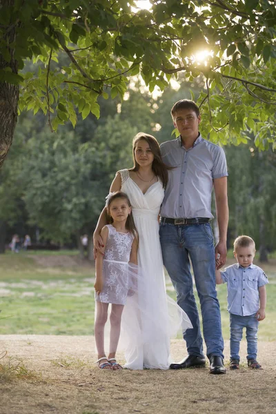 Familia sana posando en el parque verde - padre, mamá, hija y niño pequeño —  Fotos de Stock