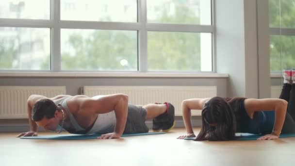 Fitnessmädchen und -mann machen gemeinsam Liegestütze im Fitnessstudio — Stockvideo