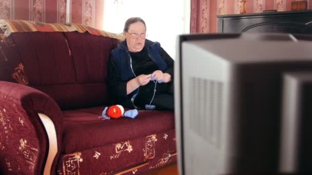 Старшая женщина смотрит телевизор вязать шерстяные носки, слайдер выстрел — стоковое видео