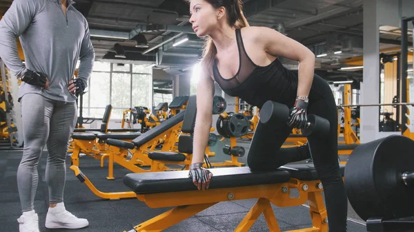 Sportlerin hebt Hanteln im Fitnessstudio - Trainer beobachtet Training — Stockfoto