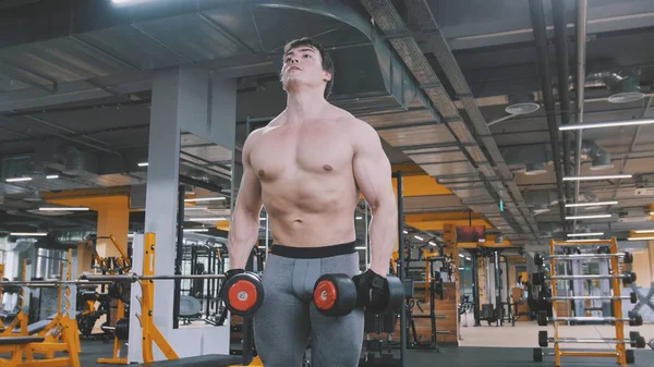 Спортсмен поднимает гантели без рубашки в спортзале — стоковое фото