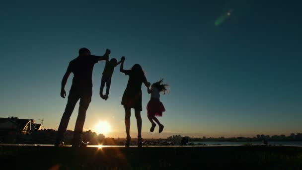 Щаслива сім'я - батько, мати, дочка і маленький син - силует на заході сонця, повільний рух — стокове відео