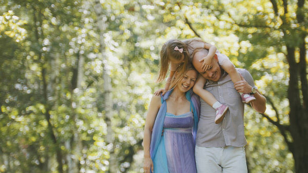 Father - bold man, mother - blonde beautiful woman and little girl - walking in the park at sunny day