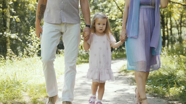 Father, mother and daughter walking in the park at sunny day