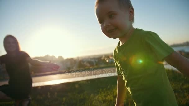 Pequeño niño caucásico jugando y riéndose con la madre en el parque al atardecer, cámara lenta — Vídeos de Stock