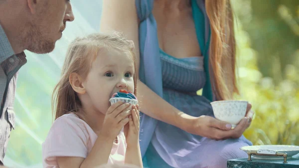 Милая блондинка ест кексы на открытом воздухе с семьей — стоковое фото