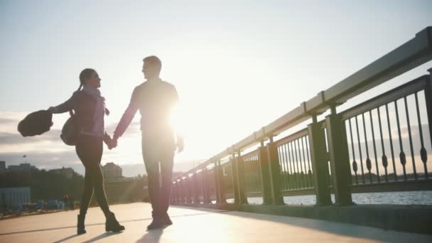 Lyckliga älskande par - pojke och flicka - vandrar längs strandpromenaden vid solnedgången — Stockvideo