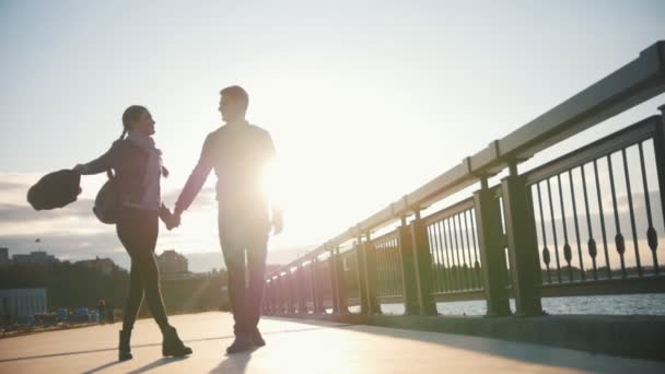 Feliz pareja amorosa - niño y niña - están caminando a lo largo del paseo marítimo al atardecer — Vídeo de stock