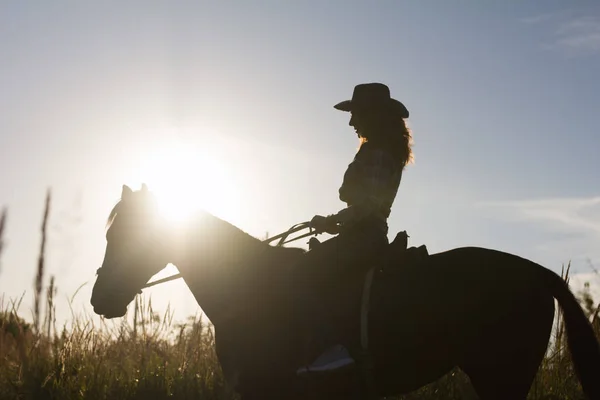 Silhouette einer Frau mit Cowboyhut auf einem Pferd - Sonnenuntergang oder Sonnenaufgang, horizontal — Stockfoto