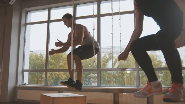 Ελκυστική κοπέλα και μυώδης άνδρας fitness εκπαιδευτή κάνει κουτί άλμα άσκηση κατά τη διάρκεια μια προπόνηση στο γυμναστήριο — Φωτογραφία Αρχείου