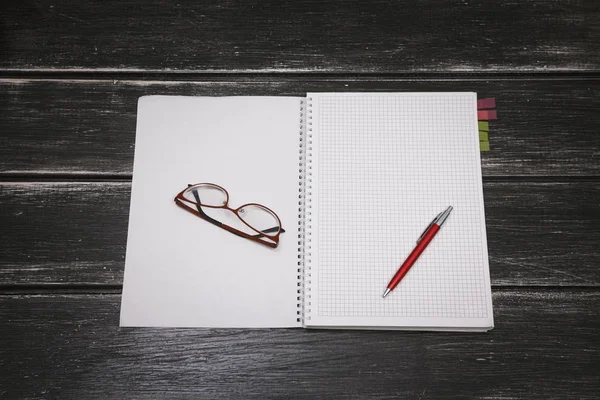 Белая тетрадь, ручка и очки на черном деревянном фоне — стоковое фото