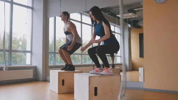 Esportivo jovem mulher e musculoso homem instrutor de fitness fazendo caixa de salto exercício durante um treino no ginásio — Fotografia de Stock