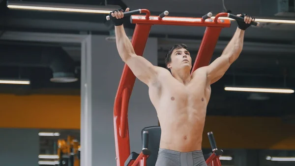 Muscular young man pulling up in a gym, close up