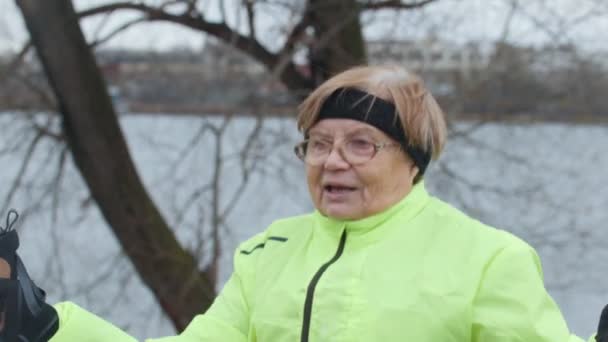 Mulher sênior em casaco verde fazendo exercícios de aquecimento ao ar livre — Vídeo de Stock