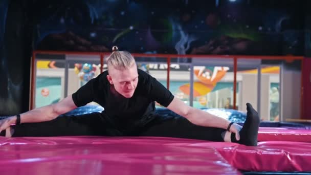 Acrobat split - jovem loira caucasiano de cabelos longos homem alongamento e aquecimento antes do treinamento acrobático em trampolim — Vídeo de Stock