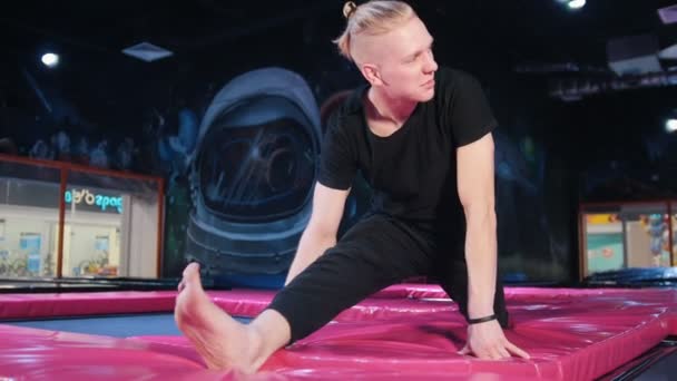 Unga blondin kaukasiska manlig stretching och uppvärmning före akrobatiska träning på studsmatta — Stockvideo