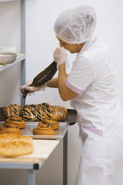 Vuxen kvinna i uniform bakar kakor i bageriet — Stockfoto