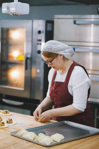 Vuxen kvinna i glasögon bakar kakor i bageriet — Stockfoto