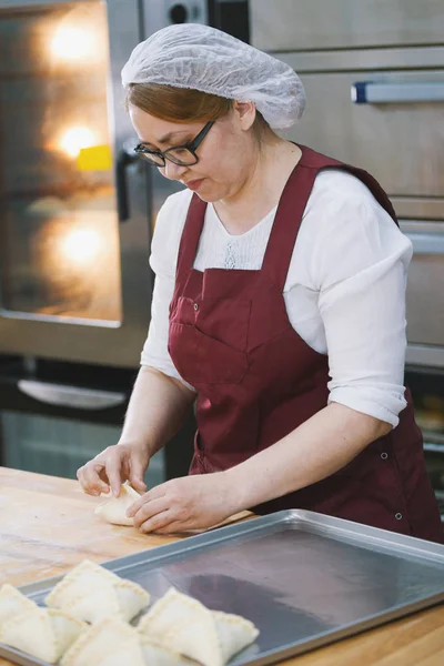 Vuxen kvinna i glasögon och förkläde bakar kakor i bageriet halv-profil — Stockfoto
