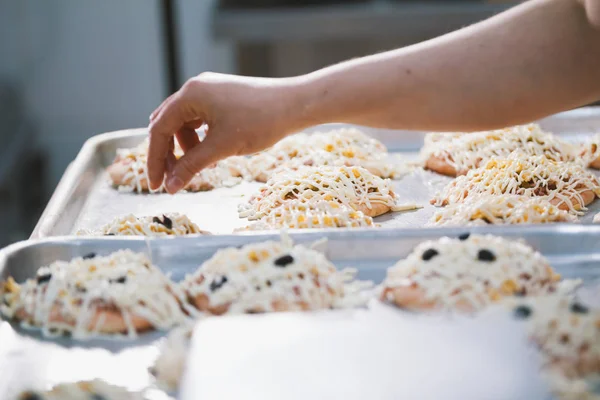 Cook puts the filling on the mini pizza in the bakery