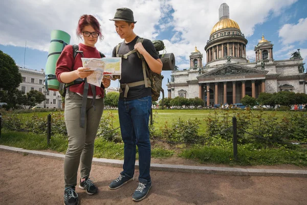 Jóvenes turistas revisan la ruta en el mapa de papel cerca de Kazan Kathedral de San Petersburgo, Rusia —  Fotos de Stock