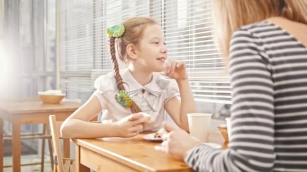 Flicka med tofsar äter söta kakor och pratar med sin mamma i caféet — Stockvideo