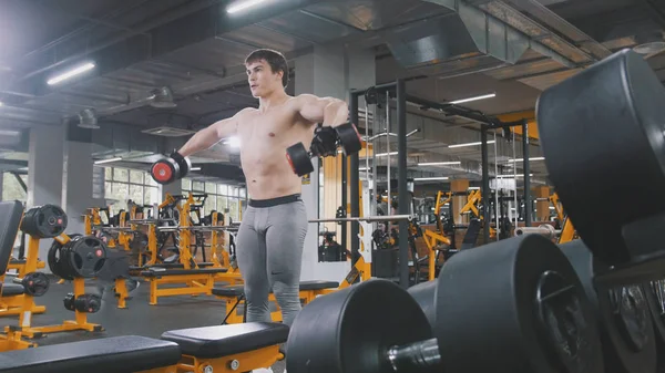 М'язистий спортсмен у спортзалі піднімає гантелі без сорочки — стокове фото
