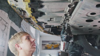 Araç otomatik Servisi - tamirci arabanın alt aracın altına detayını unscrews.