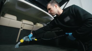 Genç adam araba iç elektrikli süpürge ile temizler