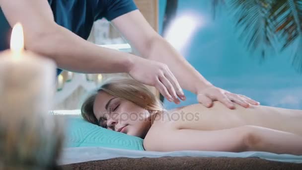 Мужские руки на спине девушки в массажном салоне — стоковое видео
