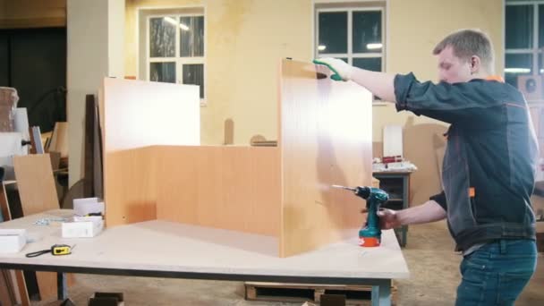 Timmerman met een elektrische schroevendraaier bezig met de fabriek, vaststelling van houten meubilair details — Stockvideo