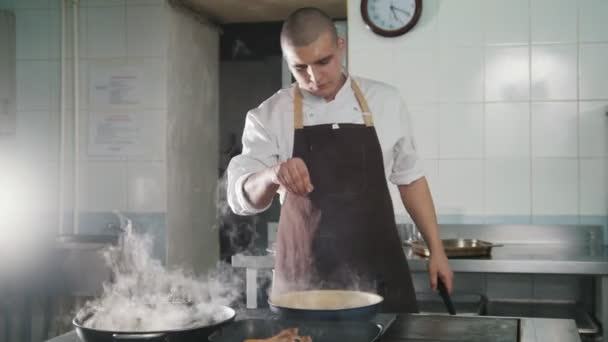 Повар добавляет специи и лук в еду — стоковое видео