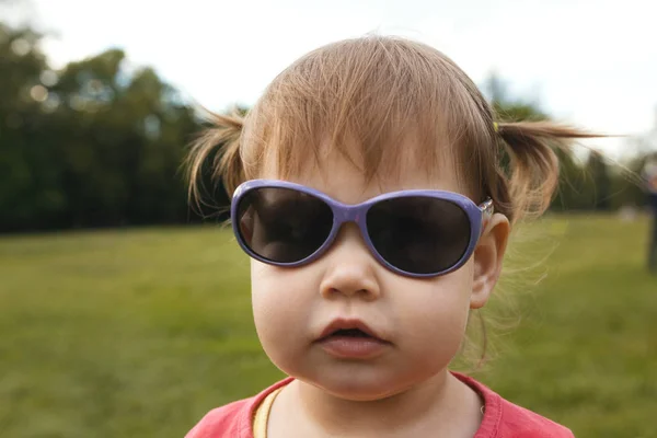 Nettes kleines Mädchen mit Sonnenbrille im Park vor grünem Gras — Stockfoto