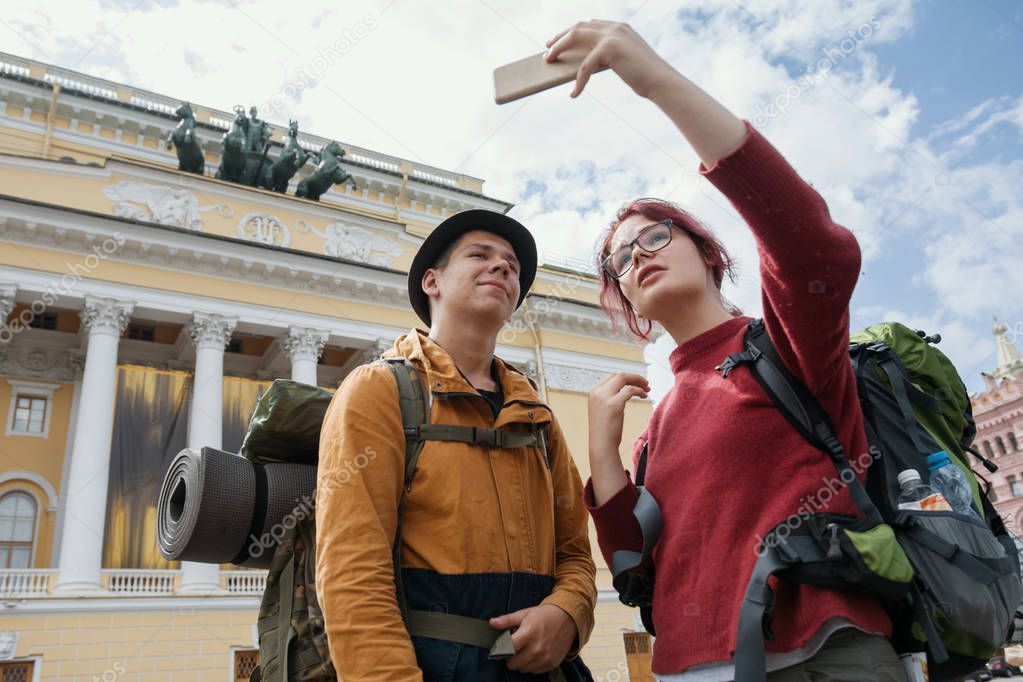 Young man and teenager girl - tourists - taking selfies against the Bolshoi theatre in Saint-Petersburg, Russia