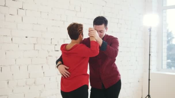 Frau mittleren Alters und junger Mann in rotem Hemd tanzen Kizomba im Studio — Stockvideo