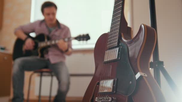 Junger attraktiver Mann komponiert Musik auf der Gitarre und spielt, anderes Musikinstrument im Vordergrund, verschwommenes Konzept — Stockvideo