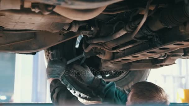 Автосервис - механик откручивает автомобильные детали во время работы под подъемником — стоковое видео