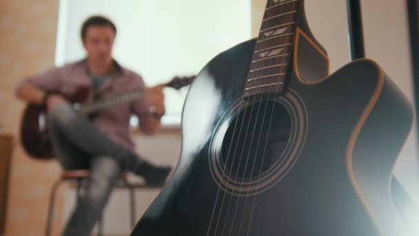 Ung attraktiv kille musiker komponerar musik på gitarr och spelar, andra musikinstrument i förgrunden suddig — Stockvideo