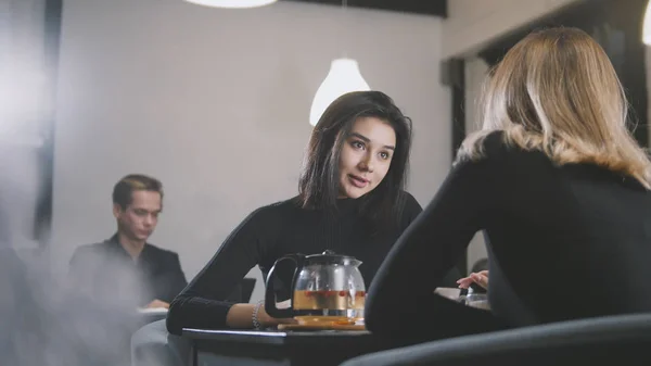 Ganska ung kvinna med svart hår talar med flickvän i caféet — Stockfoto