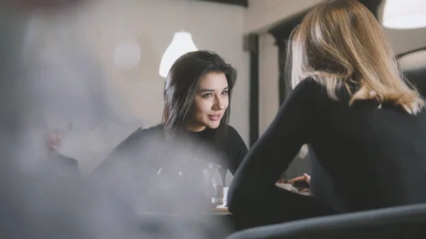 Svart haired ung kvinna med svart hår dricker kaffe och pratar med flickvän i caféet — Stockfoto