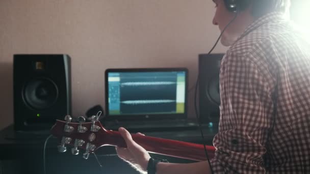 Mladý muž hudebník composes a zaznamenává soundtrack hrát na kytaru, pomocí počítače, sluchátka a klávesnice — Stock video