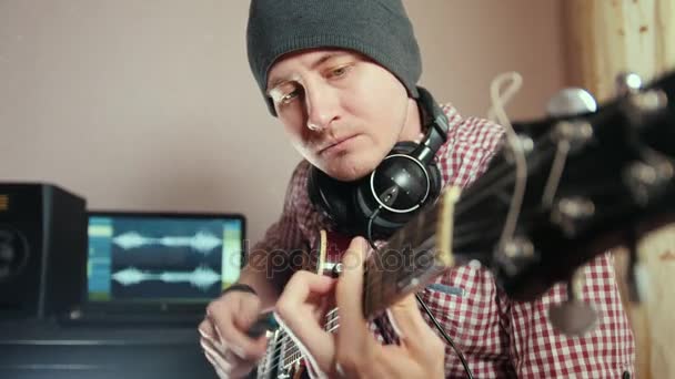 Молодий привабливий чоловічий музикант пише і записує саундтрек, граючи на гітарі за допомогою комп'ютера, зосереджуючись на обличчі і руках — стокове відео