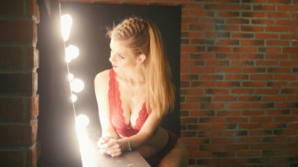 Fiatal szőke longhaired modell a vörös fehérnemű pózoló fotós közelében a világítás, során fashion photo-munkamenet — Stock videók