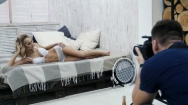 Sarışın model fotoğrafçı için poz giyinmiş beyaz iç çamaşırı, yatakta yatıyordu